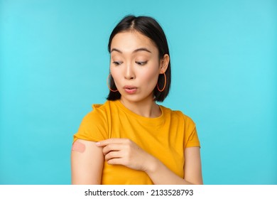 Vaccine Campaign From Covid-19. Young Beautiful, Healthy Asian Woman Showing Shoulder With Bandaid, Concept Of Vaccination, Standing Over Blue Background