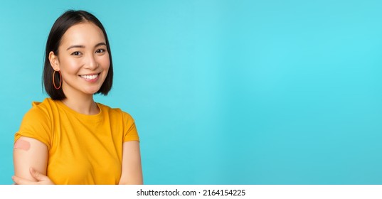 Vaccine Campaign From Covid-19. Young Beautiful, Healthy Asian Woman Showing Shoulder With Bandaid, Concept Of Vaccination, Standing Over Blue Background