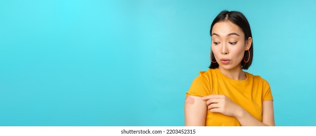 Vaccine Campaign From Covid-19. Young Beautiful, Healthy Asian Woman Showing Shoulder With Bandaid, Concept Of Vaccination, Standing Over Blue Background