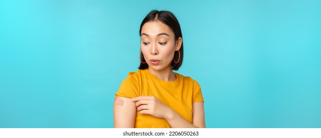 Vaccine Campaign From Covid-19. Young Beautiful, Healthy Asian Woman Showing Shoulder With Bandaid, Concept Of Vaccination, Standing Over Blue Background