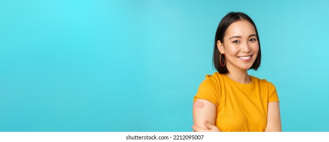 Vaccine Campaign From Covid-19. Young Beautiful, Healthy Asian Woman Showing Shoulder With Bandaid, Concept Of Vaccination, Standing Over Blue Background