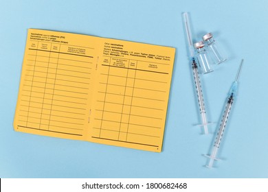 Vaccine Concept With Syringes, Vials And Empty Yellow International Certificate Of Vaccination With German And English Text On Blue Background