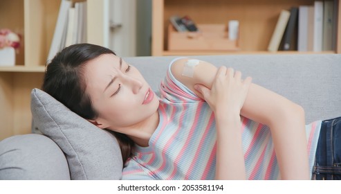 Vaccine Side Effect Concept - Asian Woman Lying On Couch Has Arm Muscle Pain Ache In Living Room At Home