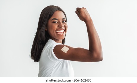 Vaccines Save Lives. Excited Happy Black Lady Showing Arm With Adhesive Bandage After Covid Antiviral Shot, Vaccinated Young Female Demonstrating Biceps With Plaster, White Studio Banner Panorama - Powered by Shutterstock