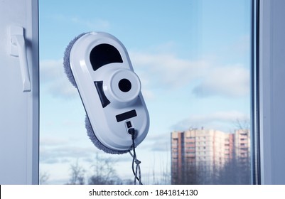 Vacuum Cleaner Robot Washing Glass Window. Blue Sky And Building Background. Robot Assistant At Home For Cleaning Windows.