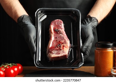 Vacuum packaging of fresh marinated beef in the hands of a cook on a black background. - Shutterstock ID 2235770847