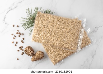 Vacuum packaging of shelled cedar pine nuts with cones and evergreen branch on marble background. Top view supermarket product in transparent package.