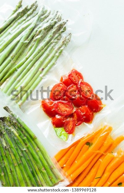 Vacuum sealed vegetables , carrots, asparagus,\
tomatoes,  on a gray background top view, ready to be cooked with\
sous vide rooner