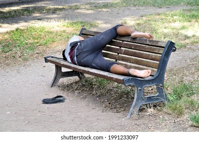 a vagabond taking a nap on a public bench in a strange way