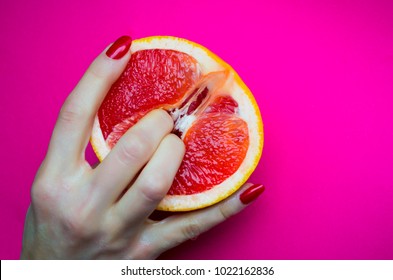 Vagina symbol. Two fingers on grapefruit on pink background. Sex concept.