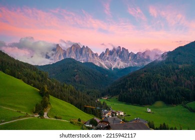 Val di Funes valley with amazing alpine Dolomites covered with pink clouds at sunset and Santa Maddalena village on the hill. 