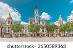 Valencia City Hall (Ajuntament de Valencia) timelapse hyperlapse in Plaza de Ayuntamiento. Historic building with clock tower under a blue cloudy sky. People strolling the main square in Spain