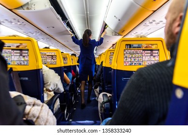 Valencia, Spain - March 8, 2019: Stewardess Inside A Ryanair Plane Securing The Top Luggage Before Takeoff, Walking Down The Aisle From Behind.