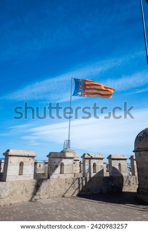 Valencia, Spain - May 12 2023 : The city of valencia community flag flys high above the portal quart towers on a bright sunny day. vertical portrait mobile format