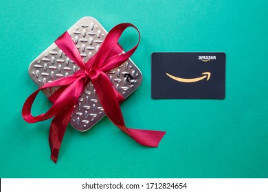 Valencia/Spain: 04.23.2020: Close Up Of A Amazon Spain Gift Card 2020 With Metallic Box And Red Beautiful Gift Bow. Green Background. Concept Of E-commerce.