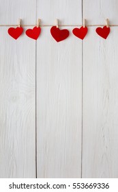Valentine background with red paper hearts row border on clothespins on white rustic wood planks. Happy lovers day card mockup, copy space - Shutterstock ID 553669336