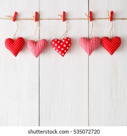 Valentine background with sewed pillow hearts row border on red clothespins at rustic white wood planks. Happy lovers day card mockup, copy space
