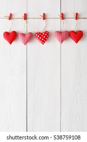 Valentine Background With Sewed Pillow Hearts Row Border On Red Clothespins At Rustic White Wood Planks. Happy Lovers Day Card Mockup, Copy Space, Vertical Composition