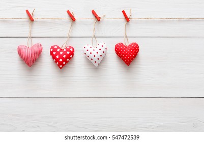 Valentine Background With Sewed Pillow Hearts Row Border On Red Clothespins At Rustic White Wood Planks. Happy Lovers Day Card Mockup, Copy Space