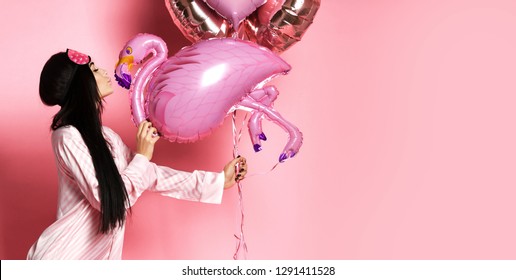 Valentine Beauty girl hold red and pink air balloons hearts blow kiss on pink background. Beautiful Happy Young woman holiday party joyful having fun celebrating Valentine's Day