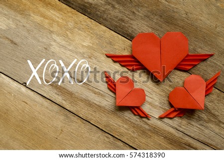 Valentine concept. Red paper origami heart with wings with XOXO written on wooden background.