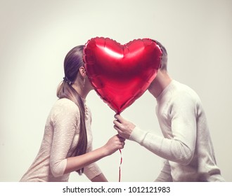 Valentine Couple. Beauty Girl and her Handsome Boyfriend holding heart shaped air balloon and kissing. Happy Joyful Family. Love. Happy Valentine's Day