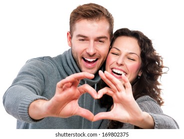 Valentine Couple. Portrait of Smiling Beauty Girl and her Handsome Boyfriend making shape of Heart by their Hands. Happy Joyful Family. Love Concept. Heart Sign. Laughing Happy Lovers. Valentines Day