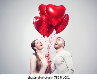Valentine Couple. Portrait of Smiling Beauty Girl and her Handsome Boyfriend holding bunch of heart shaped air balloons and laughing. Happy Joyful Family. Love. Happy Valentine's Day