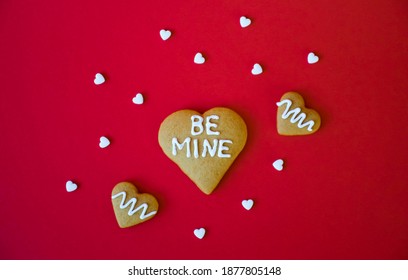 Valentine``` Day greeting card, homemade heart shaped cookies with Be Mine phrase and white candy confetti on red background. Romance and love, engagement or wedding.
