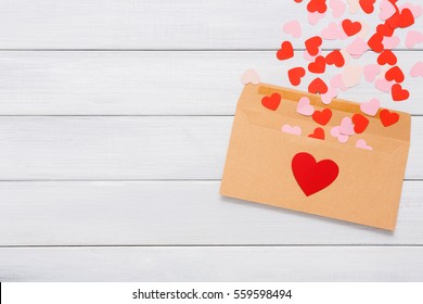 Valentine Day Love Letter. Envelope From Craft Paper With Red Hearts Heap Spread On White Wood Background. Lover's Holiday Confession Or Proposal Concept