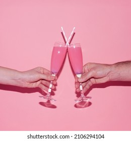 Valentine Day Party Concept. Male And Female Hand Raise Champagne Glasses With Pink Drink And Tubes And Toast On The Pink Background. Love Creative Minimal Idea