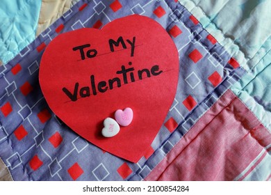 Valentine Heart Candy And A Homemade Valentine Made Of Construction Paper On A Quilt Background, Shallow Focus On Paper Valentine