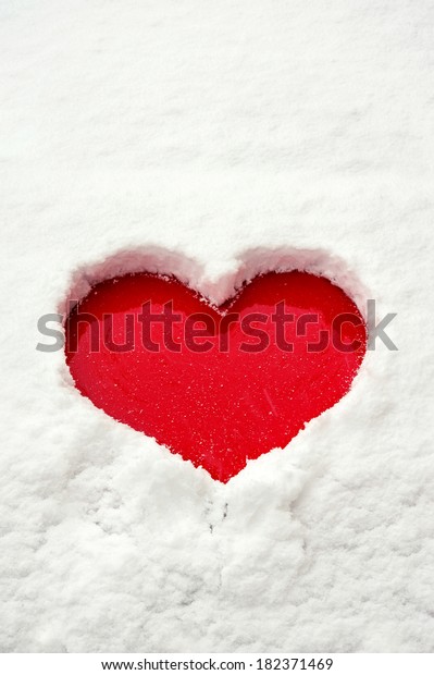 Valentine love red heart shape in snow on red\
car hood. Outdoors.\
Closeup.