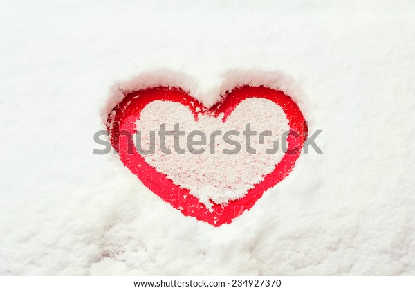 Valentine love red heart shape in snow on red\
car hood. Outdoors.\
Closeup.
