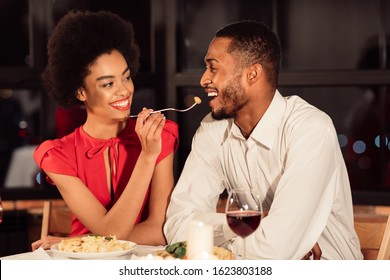 Valentine's Date. Cheerful African American Couple Feeding Each Other Having Romantic Dinner In Fancy Restaurant.