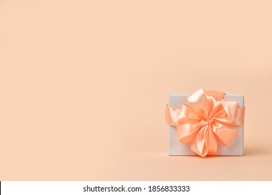 Valentine's Day background. Valentines day concept. Happy Womens day template design. Decorative white gift box with peach bow on pastel coral background. Copy space