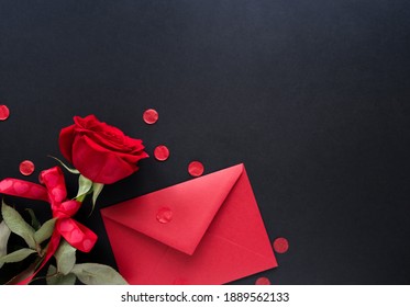 Valentines day background. Red flowers of rose and envelop on black background, top view, copy space