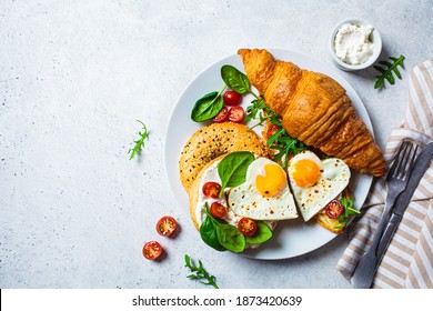 Valentine's day breakfast concept. Sandwich with croissant, bagel, cream cheese and fried eggs hearts on a white plate.