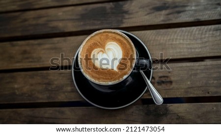 Valentines Day Cappuccino. Milk foam Heart Coffee. Coffee with heart in black mug and dish with spoon on wooden table.