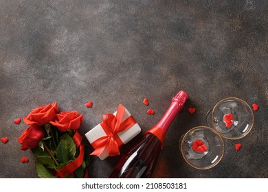 Valentine's day card with sparkling wine or champagne, red gift and red roses. View from above. Copy space.