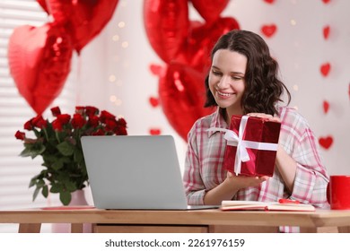 Valentine's day celebration in long distance relationship. Woman holding gift box while having video chat with her boyfriend via laptop at home - Powered by Shutterstock