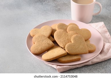 Valentine's Day coffee with milk and heart shaped cookies on pink plate on gray background. Close up. Space for your greetings.