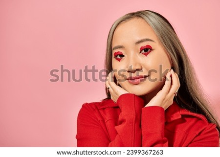 Valentines day concept, cute asian young woman with heart eye makeup posing in red jacket on pink