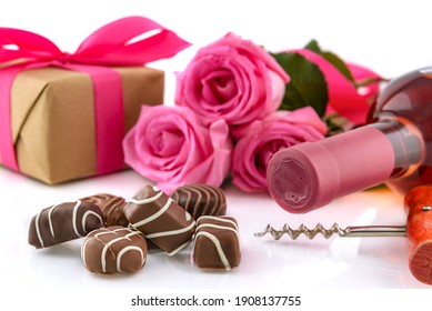 Valentine's Day concept. Delicious chocolate pralines, wine bottle, corkscrew, pink roses and gift box on a white background. Selective focus.