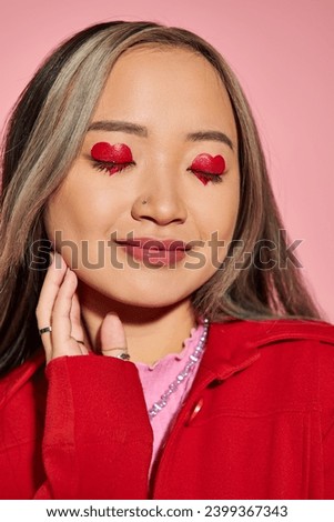 Valentines day concept, happy asian woman with heart shaped eye makeup and closed eyes on pink