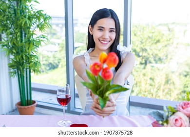 Valentine's day concept, Happy of smiling Asian young female sitting at a table food holding a fake flower vase at in the restaurant background