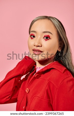 Valentines day concept, pretty asian young woman with heart eye makeup posing in red jacket on pink