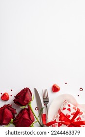 Valentine's Day concept. Top view vertical photo of bouquet of red roses heart shaped plate with giftbox candies knife fork and confetti on isolated white background with empty space - Shutterstock ID 2244463379