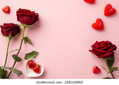 Valentine's Day concept. Top view photo of red roses heart shaped candles and saucer with chocolate candies on isolated pastel pink background with copyspace - Shutterstock ID 2245150003