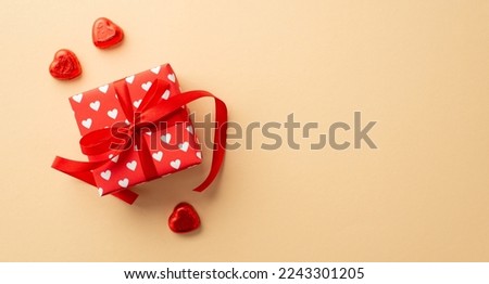 Valentine's Day concept. Top view photo of red present box in wrapping paper with heart pattern and chocolate candies on isolated pastel beige background with empty space
